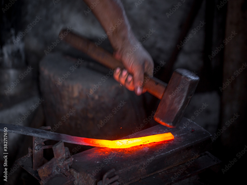 Blacksmith's hands at work. In one hand a hammer, in the other a workpiece of hot metal. Master methodically hammer hits the anvil. An example of the hard work of ancient crafts. Blacksmith's hands at work. In one hand a hammer, in the other a workpiece of hot metal. Master methodically hammer hits the anvil. An example of the hard work of ancient crafts.