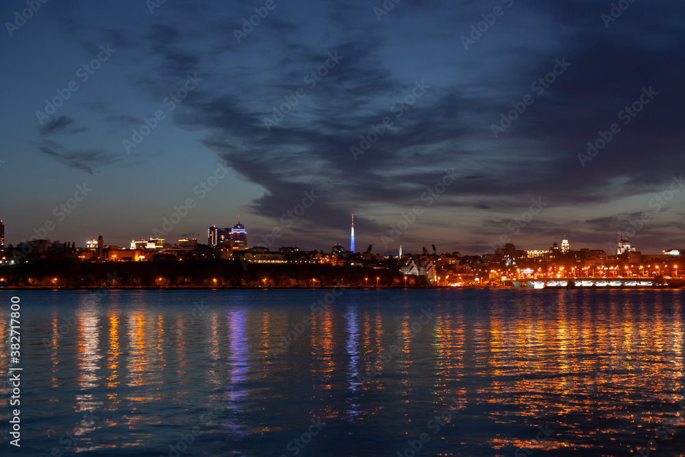 Night city against the sky, a wide river in the foreground