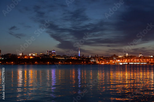 Night city against the sky, a wide river in the foreground © glavbooh