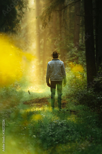 Man in denim jacket in forest during dreamy sunrise with sun rays shining trough the forest. © valdisskudre