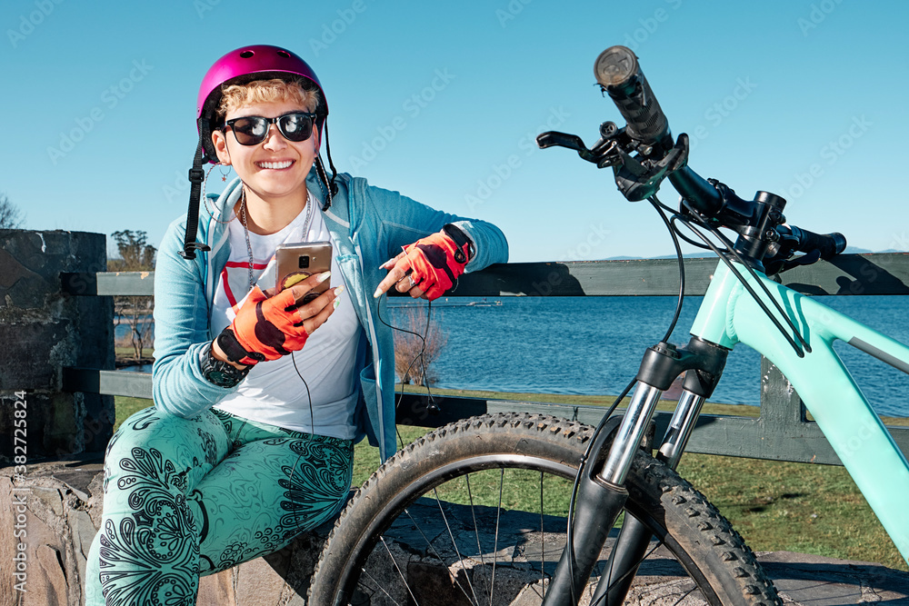 Young woman in sportswear resting next to her bike looking at her mobile phone