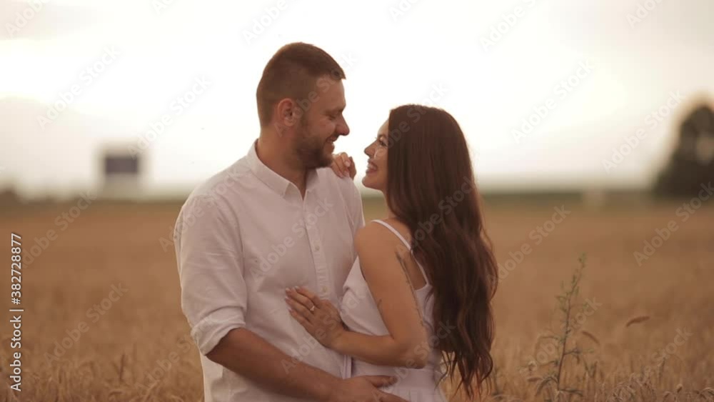 Chherful woman with long dark hair in white dress hugs with her boyfriend in white shirt on a field Chherful woman with long dark hair in white dress hugs with her boyfriend in white shirt on a field