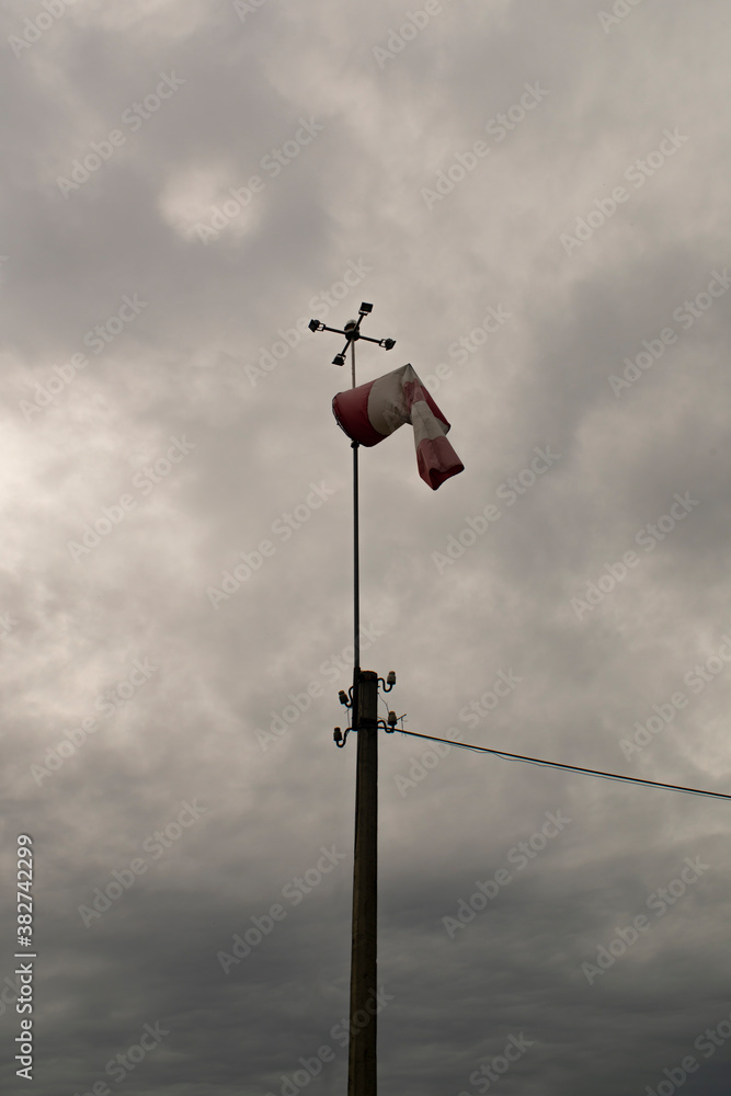 Weather station with a wind vane against the backdrop of a cloudy sky.
