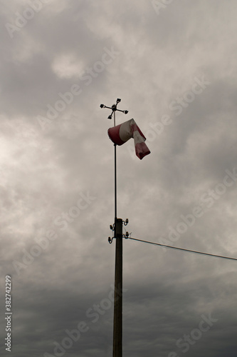 Weather station with a wind vane against the backdrop of a cloudy sky.