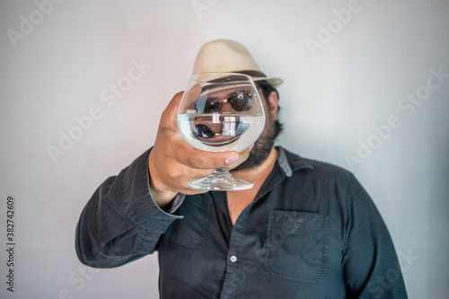 Hispanic man showing glass with clear liquor, like crystal tequila, vodka or mezcal