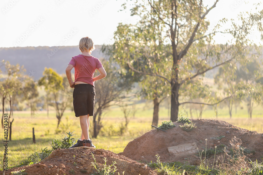 Young boy standing on dirt hill looking at scenery on remote country property