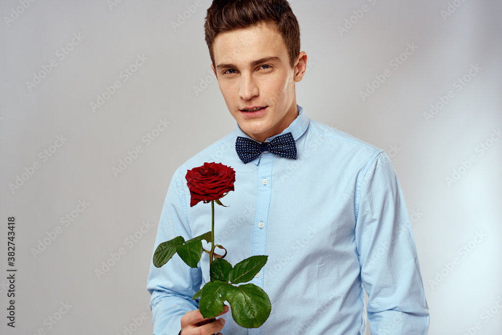 Handsome man with red rose blue shirt bow tie light background cropped view Handsome man with red rose blue shirt bow tie light background cropped view
