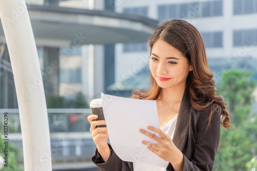 Happy business woman walking outside office with paper sheet and coffee cup in hand. Free Download Happy business woman walking outside office with paper sheet and coffee cup in hand. - GFXLoad