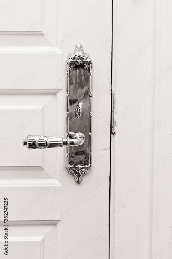 Vertical black & white antique brass Turino lever door knob on white door of historic, old Galveston Island, Texas hotel