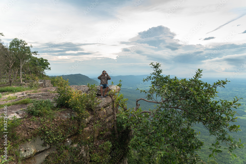 
a man sitting on the edge of the high cliffCliff with beautiful views and steep cliffs of Hua Nak at Chaiyaphum Thailand