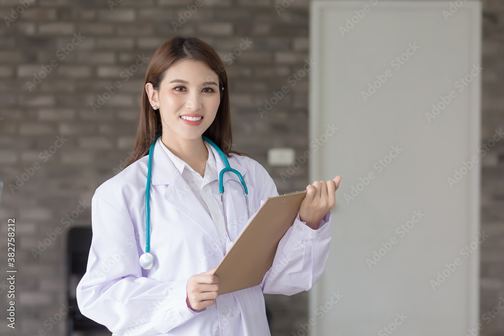Young beautiful Asian woman doctor working at hospital. She wear a white robe and stethoscope and hold a clipboard in her hands. Young beautiful Asian woman doctor working at hospital. She wear a white robe and stethoscope and hold a clipboard in her hands.