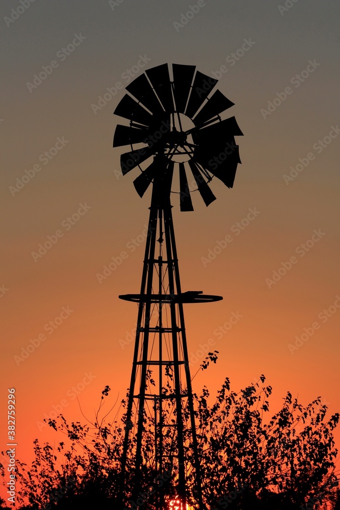 windmill at sunset with a tree silhouette out in the country north of Hutchinson Kansas USA. windmill at sunset with a tree silhouette out in the country north of Hutchinson Kansas USA.