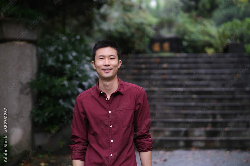 medium shot of one young Asian man looking at camera and smile, in natural park