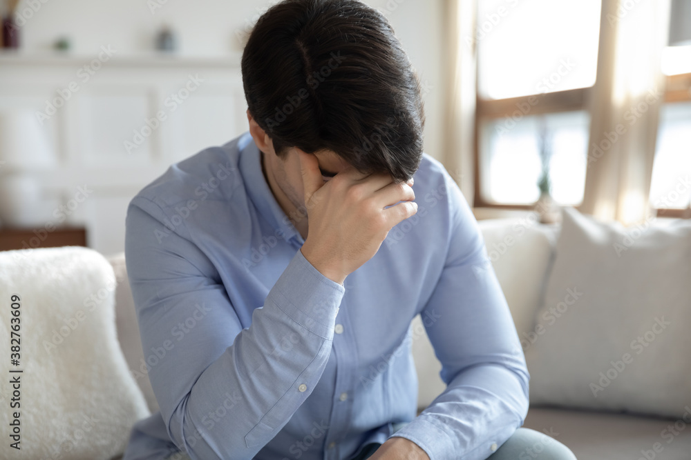 Bad day. Tired overworked millennial young male sitting on couch at home stressed and exhausted by problems in work and personal life, depressed of breakup, feeling terrible headache, migraine attack Bad day. Tired overworked millennial young male sitting on couch at home stressed and exhausted by problems in work and personal life, depressed of breakup, feeling terrible headache, migraine attack