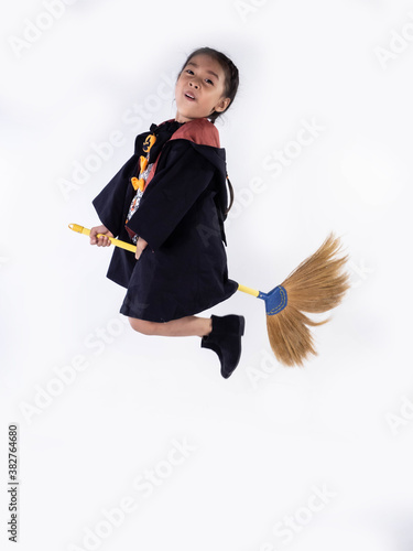 Asian children girl in witch dress costume Riding a broom for Halloween decoration in white background