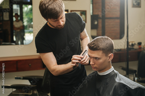 Presision work from hairdresser combing young man's hair in a barber shop photo