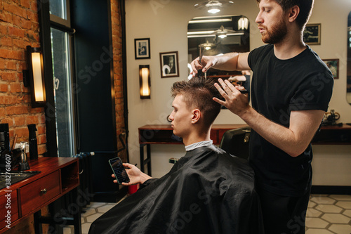 Hardworking hairdresser making a haircut for a young man in a barber shop