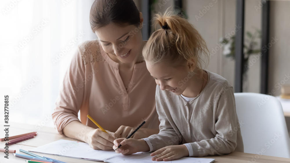 Happy young woman with little daughter drawing colored pencils, sitting at desk at home, smiling mother with pretty adorable girl child enjoying leisure time at home, creative activity Happy young woman with little daughter drawing colored pencils, sitting at desk at home, smiling mother with pretty adorable girl child enjoying leisure time at home, creative activity