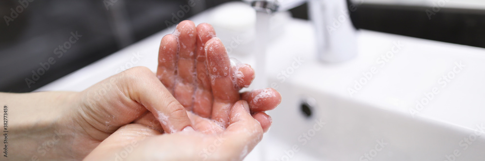 Close-up of person carefully washing hands with soap under water. Prevention infection spread. Clean white modern faucet in bathroom. Silver crane. Personal hygiene concept Close-up of person carefully washing hands with soap under water. Prevention infection spread. Clean white modern faucet in bathroom. Silver crane. Personal hygiene concept