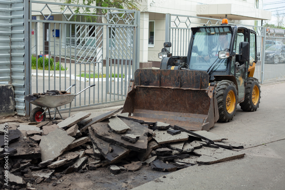 Fototapeta premium Broken asphalt is removed with a truck bucket. Road repair in the city. Removing the road surface.