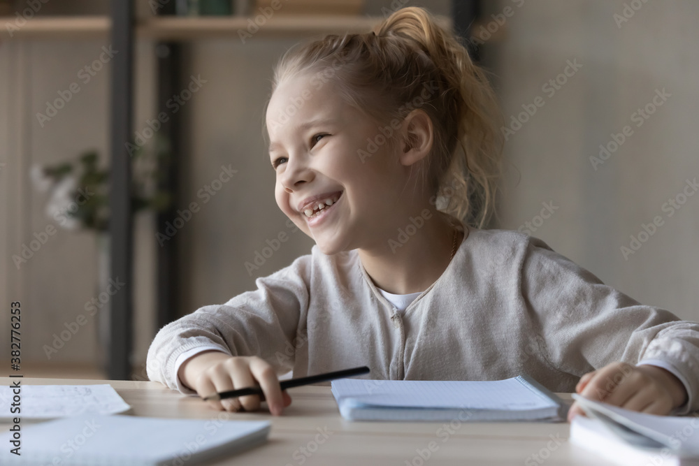 Overjoyed motivated little girl studying, doing school homework, smiling pretty child schoolgirl looking to aside, dreaming and visualizing, distracted from assignments, homeschooling concept Overjoyed motivated little girl studying, doing school homework, smiling pretty child schoolgirl looking to aside, dreaming and visualizing, distracted from assignments, homeschooling concept