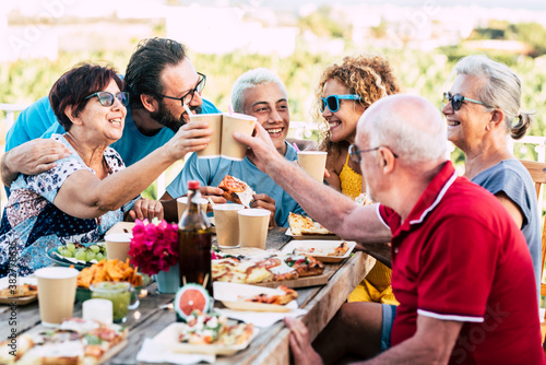 Group of caucasian family people enjoy and celebrate together in outdoor at home with country side green nature view in backgorund - senior and young friends enjoying with food and drinks