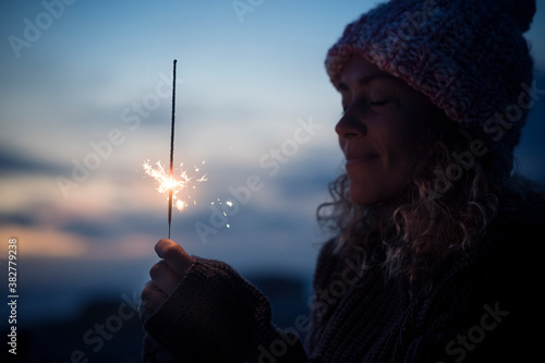 Celebration and hope future concept with beautiful woman portrait with fired sparkler in the dark of the night around - new year eve and celebration image with copy space and blue sky in background photo