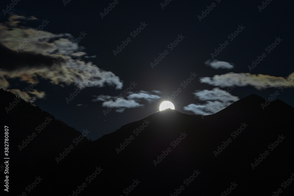 full moon rises into night sky over a mountain silhouette full moon rises into night sky over a mountain silhouette