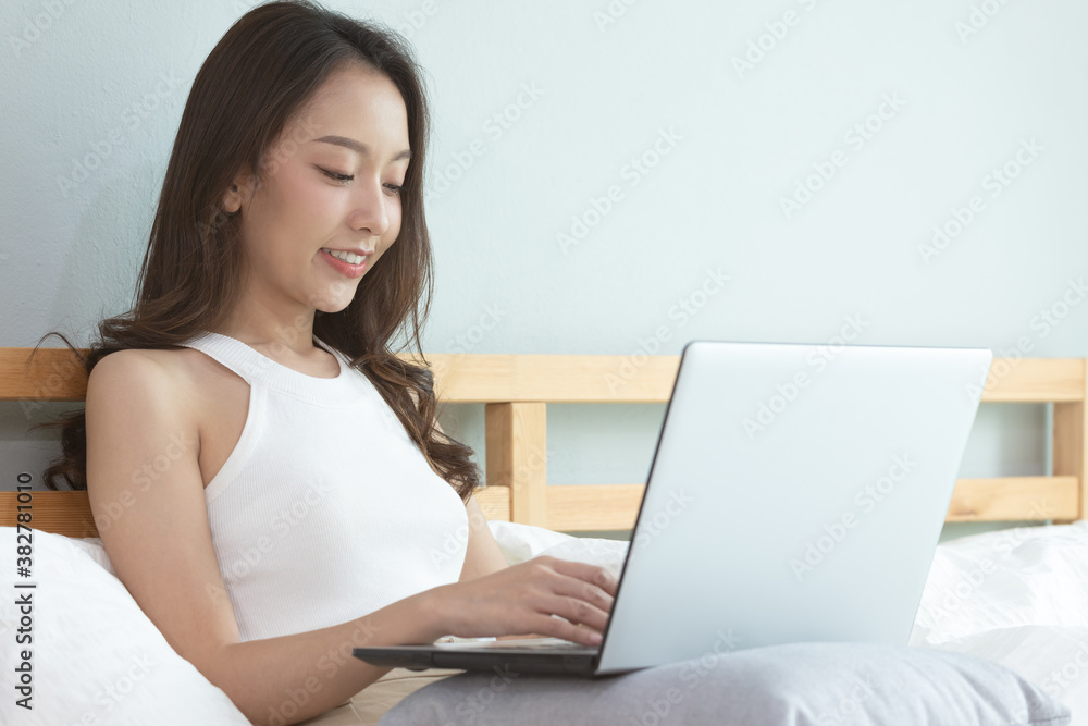 Asian woman working on a laptop sitting on the bed in the house. Asian woman working on a laptop sitting on the bed in the house.