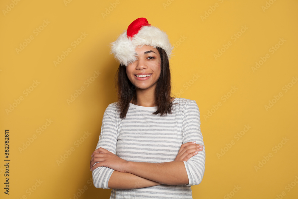 Young happy black woman in Santa hat on vibrant yellow background Young happy black woman in Santa hat on vibrant yellow background