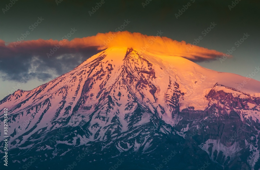 Fototapeta premium Huge snow capped Ararat Mount in the sunset in Armenia. Shining peak of the mount with orange color in clouds.
