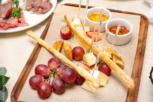 cheese plate, slices of cheese, grapes, bread, honey on the Board on the table