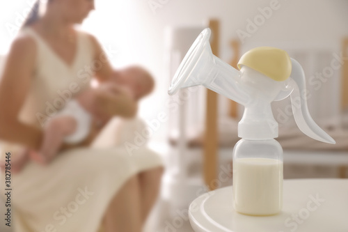 Mother and little baby indoors, focus on table with breast pump