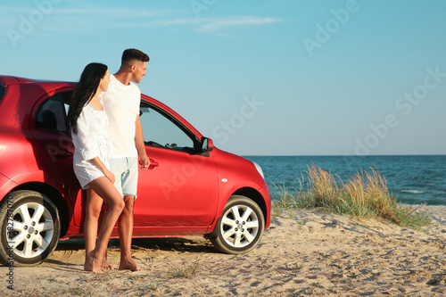 Happy couple near car on sandy beach, space for text. Summer trip © New Africa