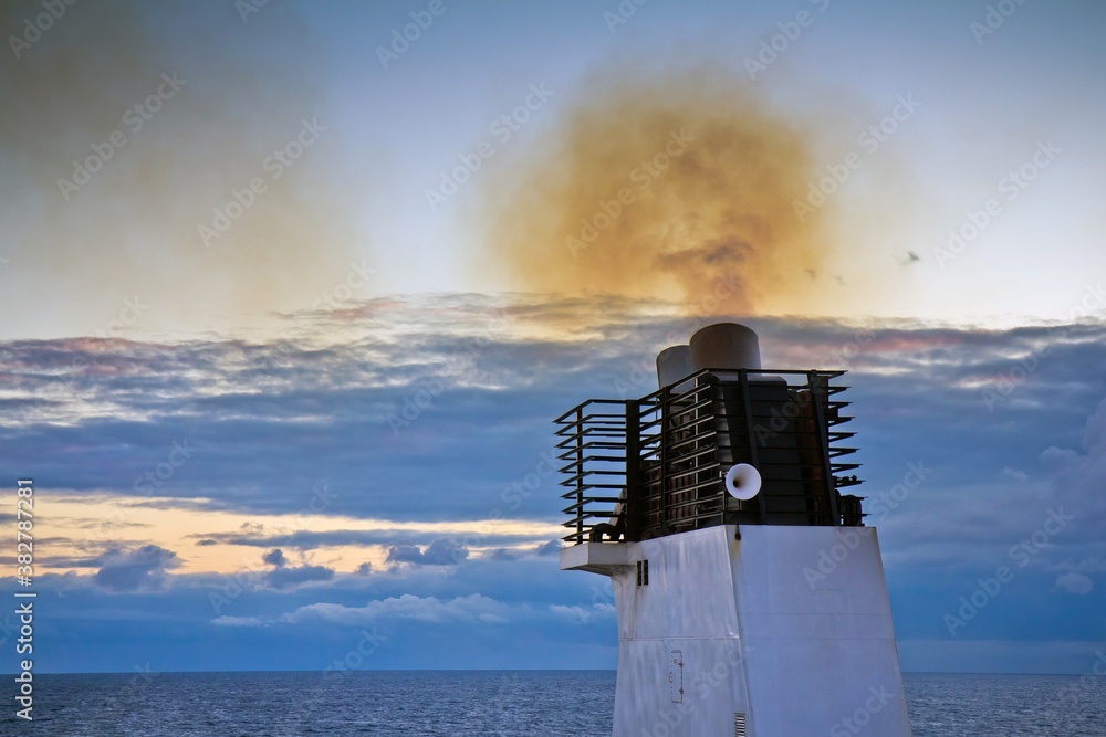 Fototapeta premium Closeup of funnel of a cargo ship floating in the Baltic sea with smoke polluting environment against cloudy sky in the evening.