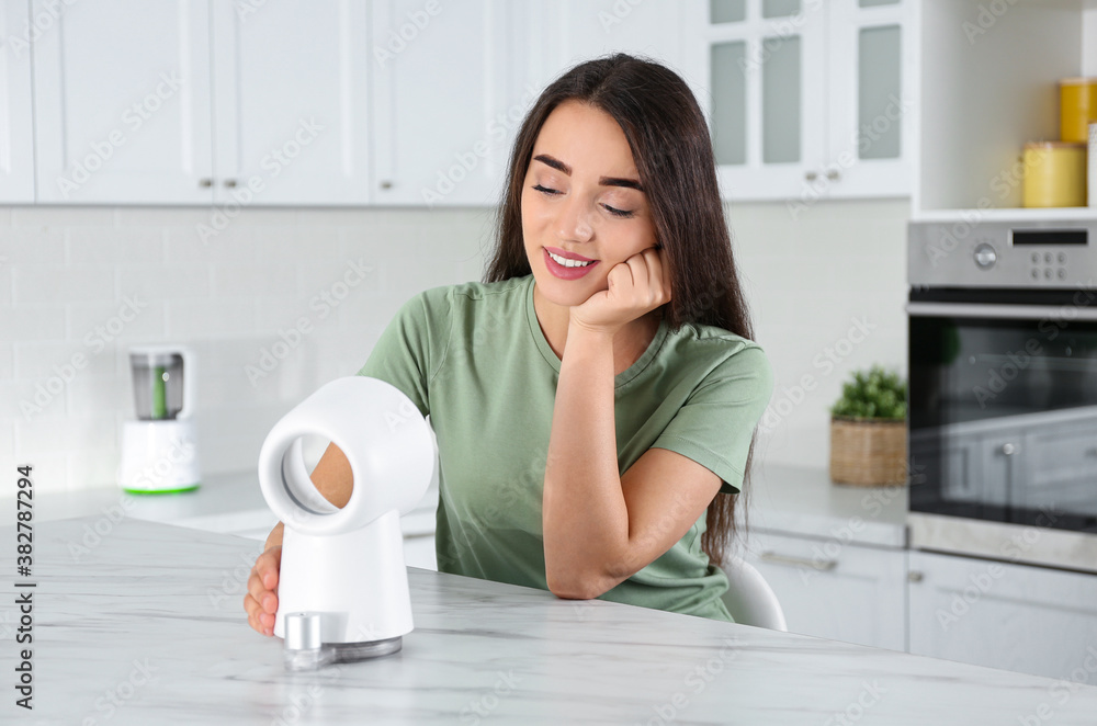 Woman enjoying air flow from portable fan in kitchen. Summer heat Woman enjoying air flow from portable fan in kitchen. Summer heat