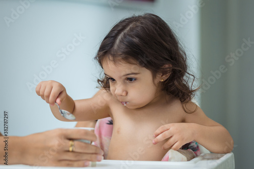 Fotografi two year old girl eats yogurt with a spoon, middle plane