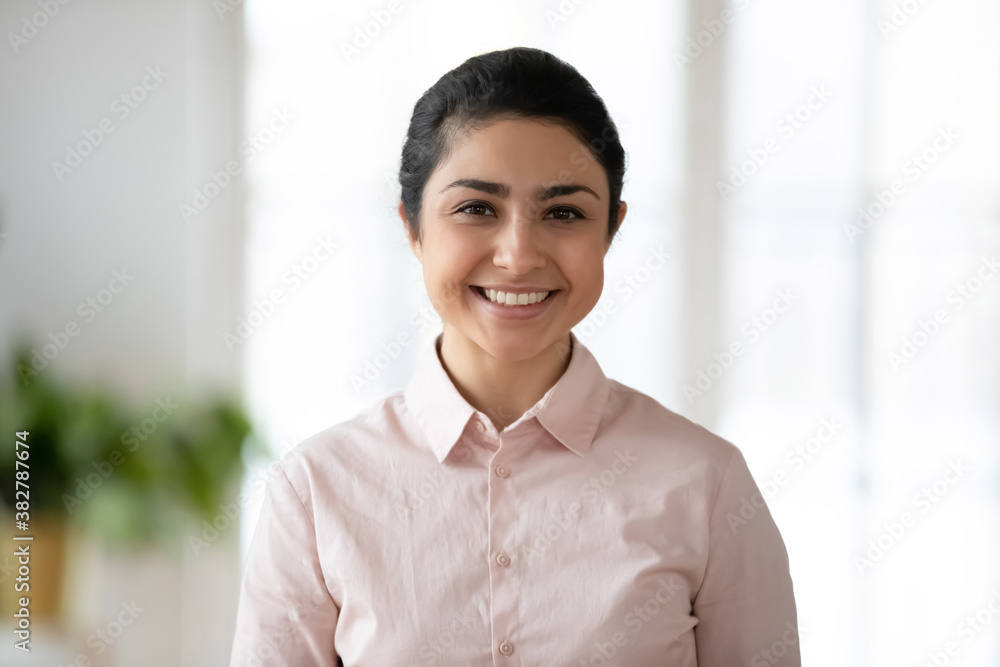 Profile picture of smiling millennial indian female employee posing in office workplace. Headshot portrait of happy confident young mixed race ethnicity company worker employer. Recruitment concept. Profile picture of smiling millennial indian female employee posing in office workplace. Headshot portrait of happy confident young mixed race ethnicity company worker employer. Recruitment concept.