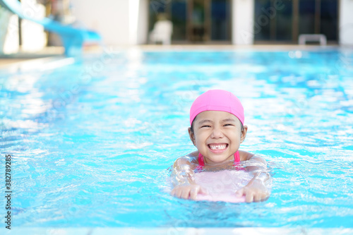 Asian child cute or kid girl wear swimming suit on swimming pool and smile with happy fun in water park for learn and training swim on kick board or refreshing and relax to exercise on summer holiday © kornnphoto