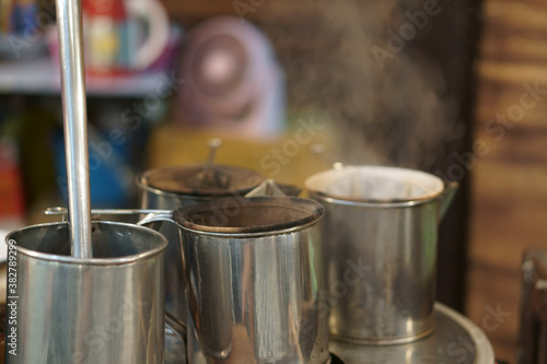 Traditional coffee dripper equipment or teh tarik and tea with aroma smoke by hot steam on old steel pot with filter cloth in cafe shop for morning drink or beverage and fresh breakfast on retro style