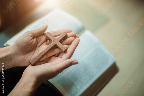 Hands pray with bible and wooden cross.
