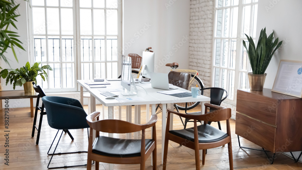 Empty modern office interior with wooden table and electronic computer gadgets on it. Loft design shared coworking workplace with no people employees or workers. Workspace area in company.