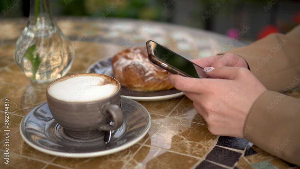 A young business woman is sitting in a cafe and texting on the phone close-up.