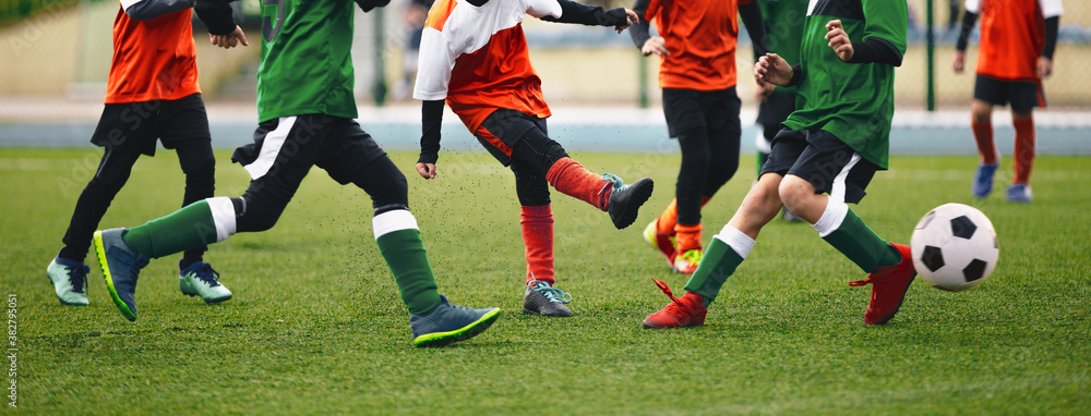 Group of children ikicking soccer ball. Kids in two football teams running after classic soccer ball. Horizntal sports background. Legs of young players on football pitch Group of children ikicking soccer ball. Kids in two football teams running after classic soccer ball. Horizntal sports background. Legs of young players on football pitch