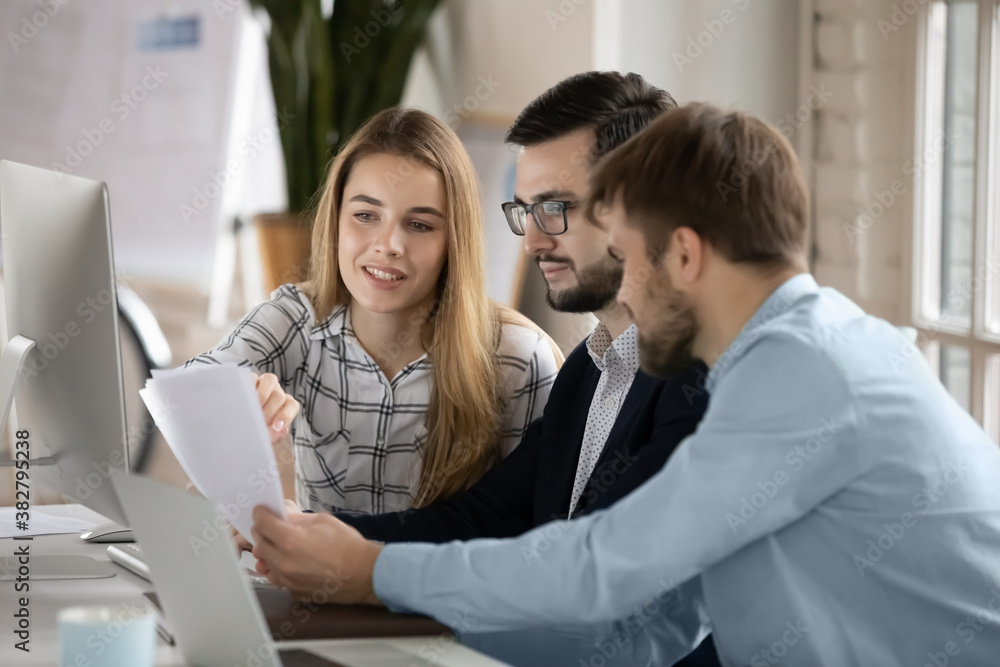 Diverse colleagues brainstorm use PC discuss company financial paperwork together. Focused businesspeople employees work cooperate on computer, consider business project. Collaboration concept.