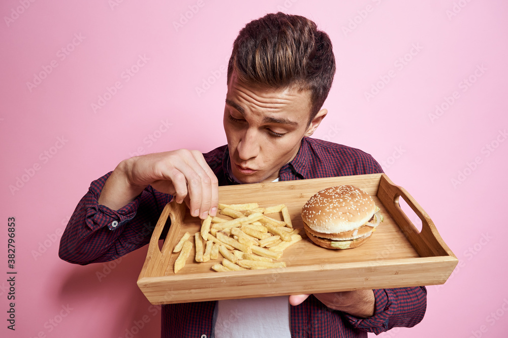 Man with fast food eating hamburger french fries pink background Man with fast food eating hamburger french fries pink background