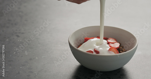 man hand pour chocolate granola with strawberries with white yogurt on a concrete countertop