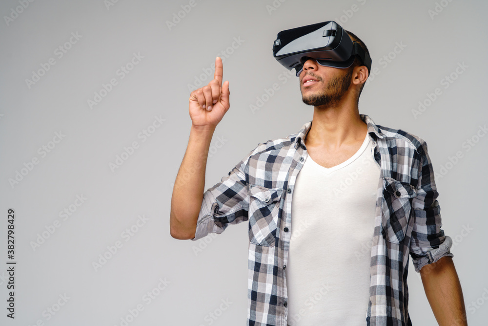 Young African-American young man wearing vr virtual reality headset over light grey background Young African-American young man wearing vr virtual reality headset over light grey background