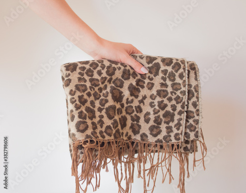  Warm autumn winter leopard scarf with fringe in the hands of a young woman. Large wide leopard print scarf