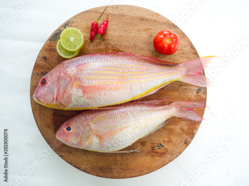 Fresh and ready to cook raw pink Perch fish with ingredients like lemon,chilli and tomatoes on a wooden pad,white background, selective focus. photo